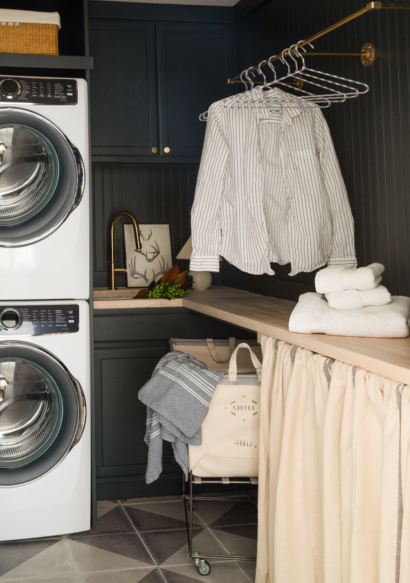 Small but functional laundry room with stackable washer & dryer, brass hanging rod and butcher block countertops to warm the space