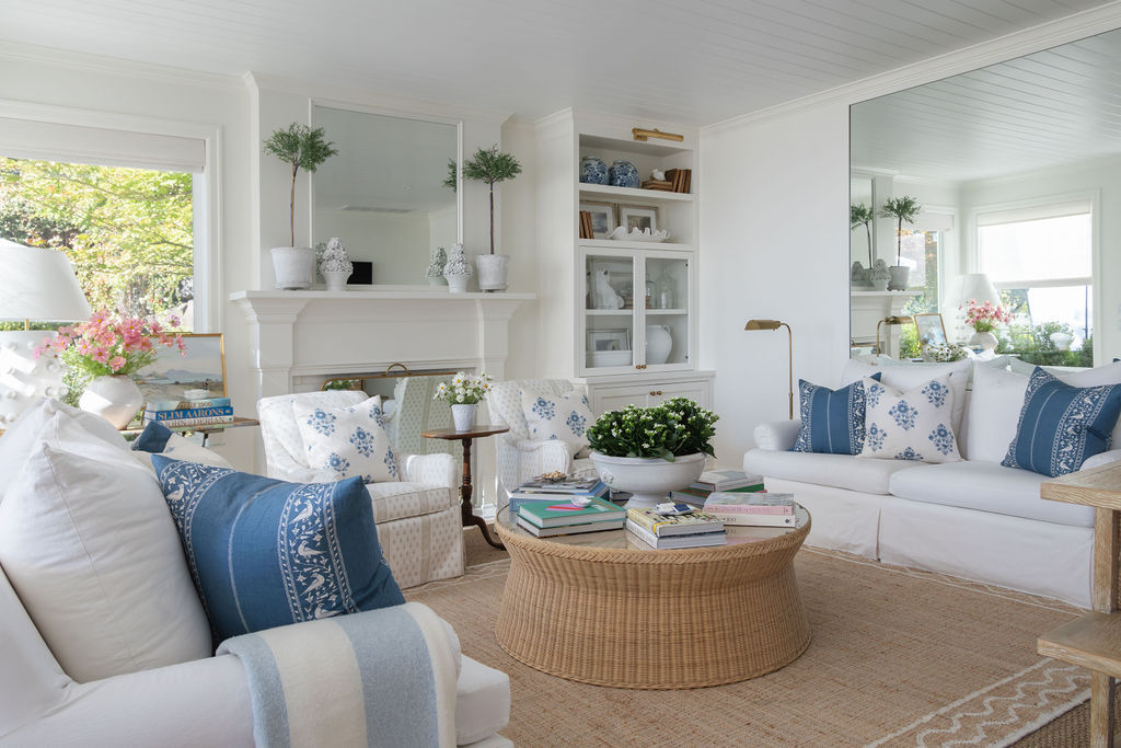 Airy living room with white sofas, blue patterned pillows, woven round coffee table, and built-ins around the fireplace.