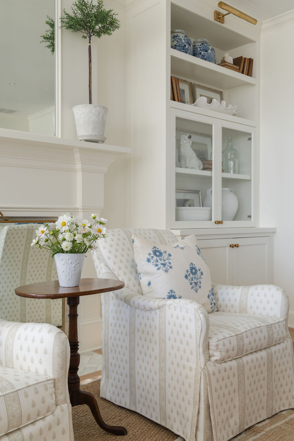 Living room vignette: block-print club chair with blue floral pillow beside a small pedestal table and built-in cabinet.