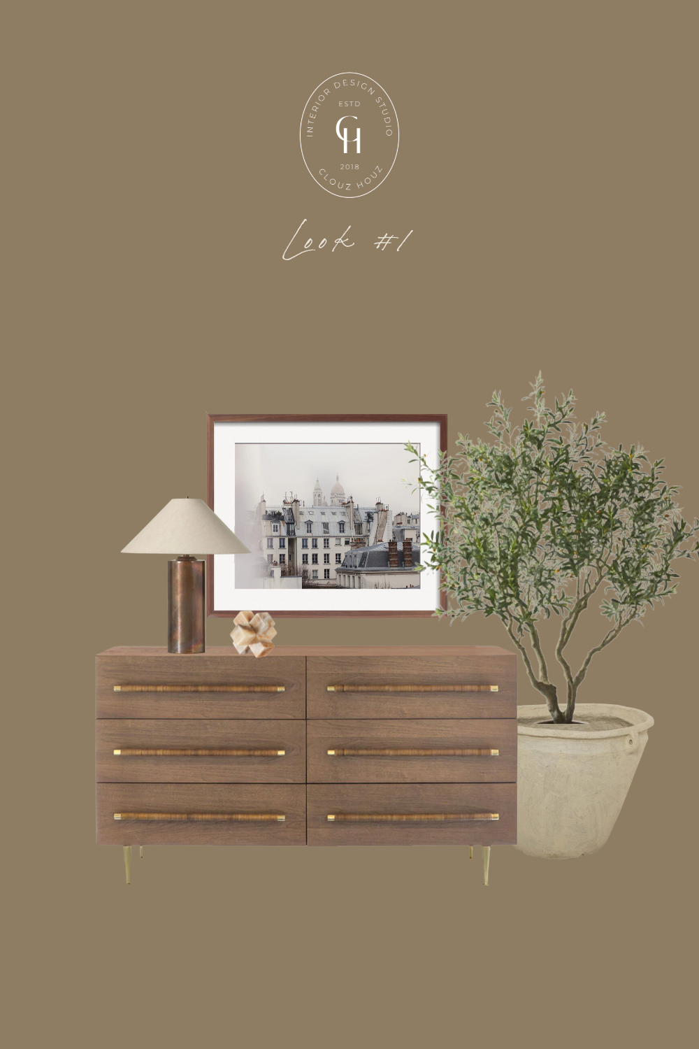 A modern wood dresser with gold hardware is styled with a bronze table lamp, a framed photograph of a Parisian rooftop, a decorative onyx sculpture, and an olive tree in a neutral stone pot, creating a cozy and elegant vignette.