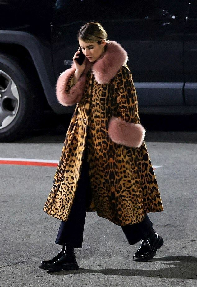 Emma Roberts walking in a bold leopard-print coat with pink fur accents, paired with dark trousers and shiny black boots. A striking street-style moment mixing fierce patterns and playful textures.
