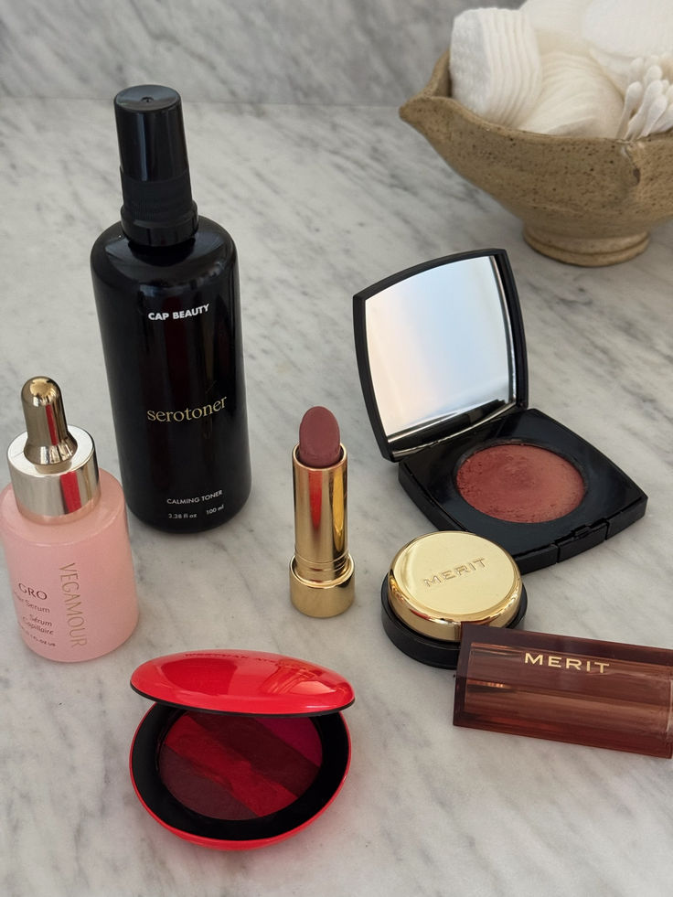 A curated selection of beauty and skincare products displayed on a marble countertop, including a calming toner, nourishing serum, and elegant blush and lipstick options. A snapshot of everyday glow-up essentials for a minimal yet polished routine.