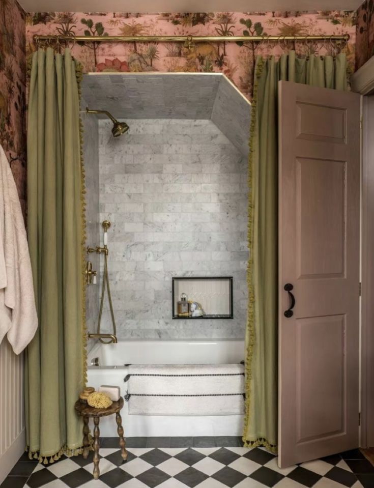 A luxurious bathroom with green tasseled shower curtains, a brass showerhead, marble tiles, and floral wallpaper. A small stool with a natural sponge adds rustic charm to the elegant, vintage-inspired space.