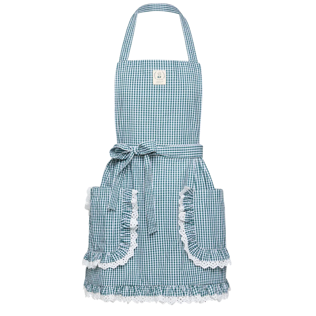 Feminine gingham apron in blue with white lace trim, ruffled pockets, and a bow tie waist.