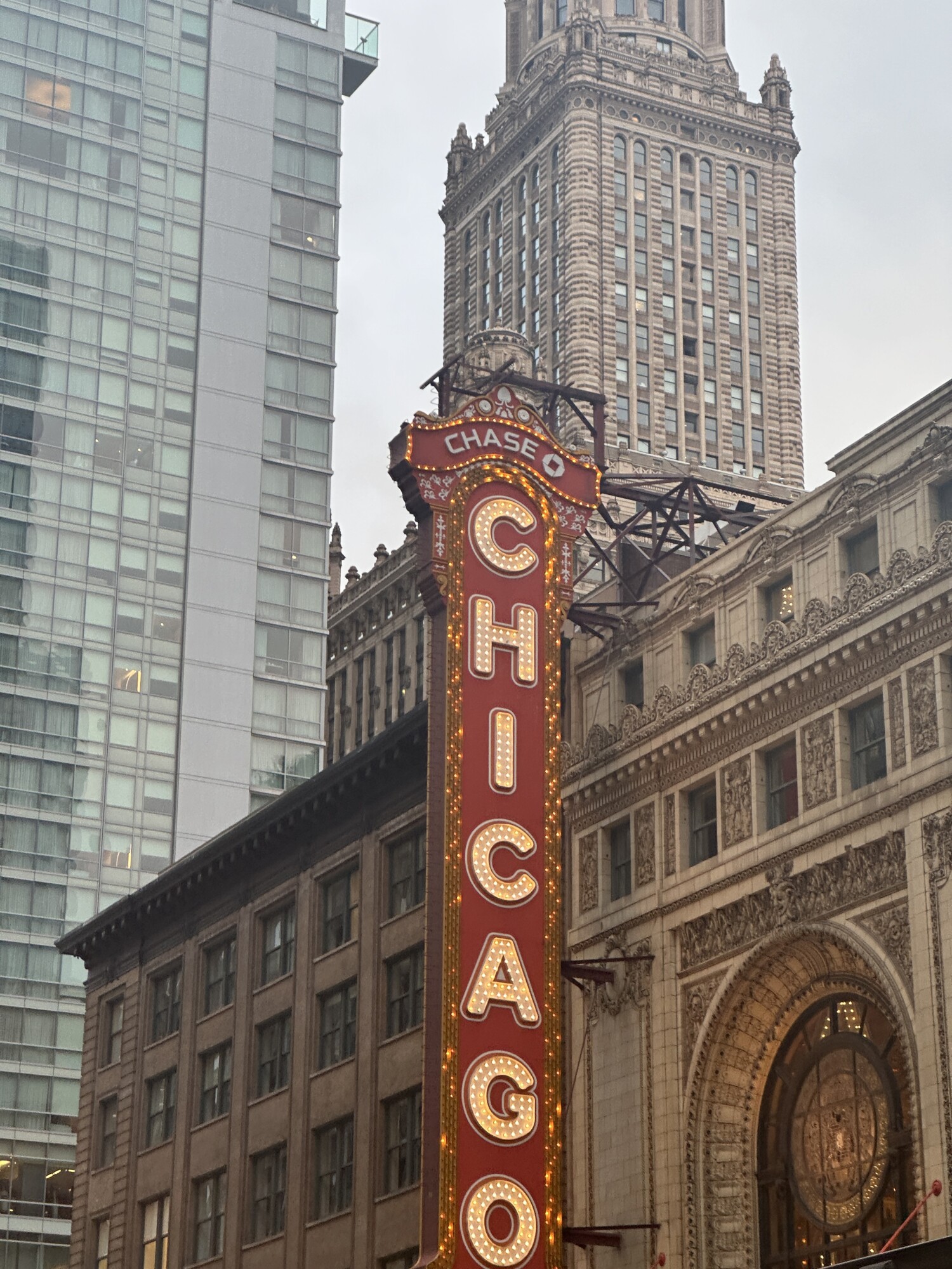 Iconic red and gold vertical “Chicago” theater sign lit up at dusk, framed by historic and modern high-rise buildings downtown.