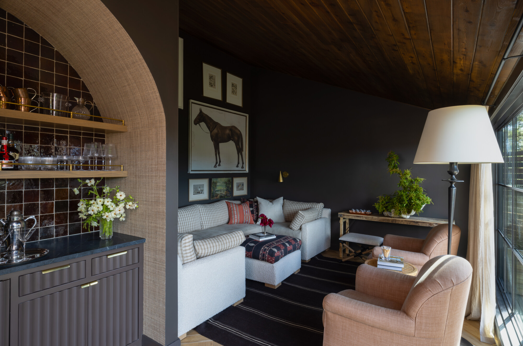 High Desert Tumalo Ranch 'Rumpus Room' landscape view of patterned secitonal sofa with a mtching ottoman in a deep, moody brown room with a vintage gallery wall above the sofa.