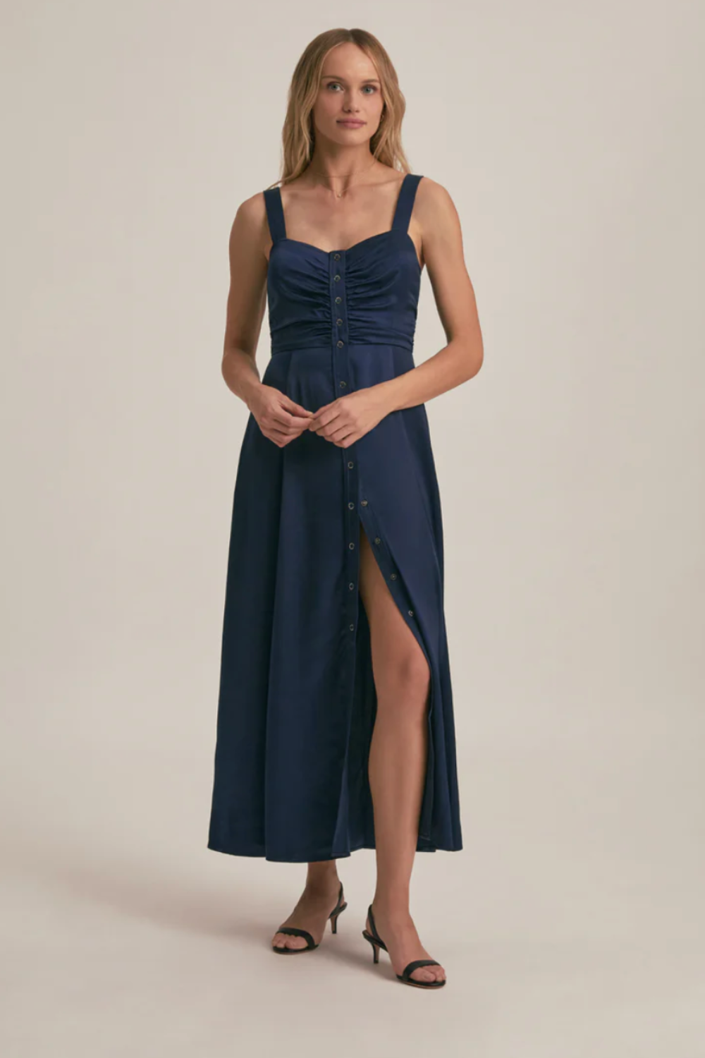 A classic, midi-length navy dress with thick straps, ruching at the bust, and a row of buttons down the center.