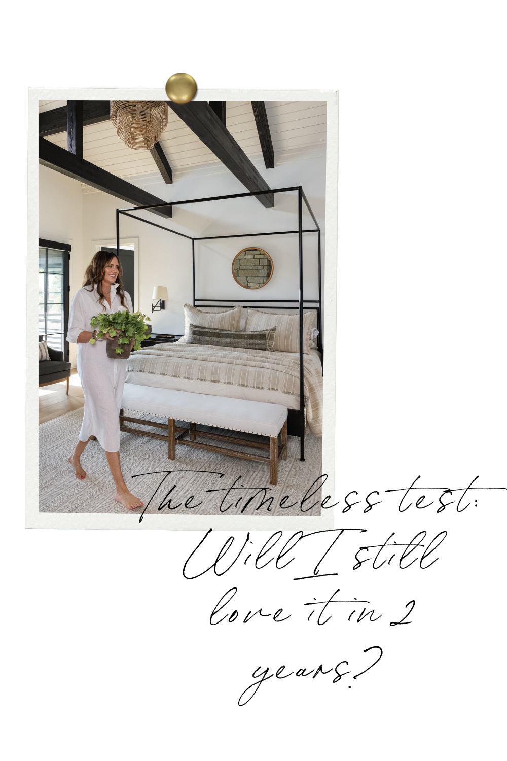 A woman in a white dress walks barefoot while holding a potted plant in a serene bedroom with a black canopy bed, neutral striped bedding, and a woven light fixture on a white vaulted ceiling with black beams. A round mirror hangs above the bed, and handwritten text reads: “The timeless test: Will I still love it in 2 years?”