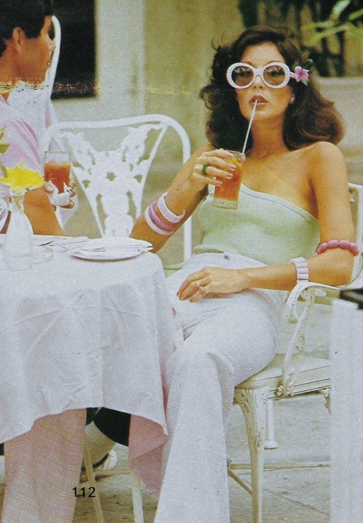 A stylish woman in retro fashion with oversized sunglasses, sipping a drink at an outdoor café table, surrounded by white wrought iron chairs and soft pink table linens.