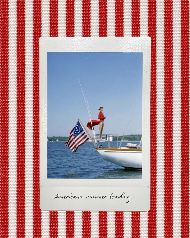 A vintage-style photo of a woman in a red swimsuit standing confidently on the bow of a sailboat, with an American flag waving behind her. The boat floats on calm blue water under a clear sky. The photo is framed like a Polaroid and set against a red-and-white striped fabric background. Handwritten text reads: “Americana summer loading…”