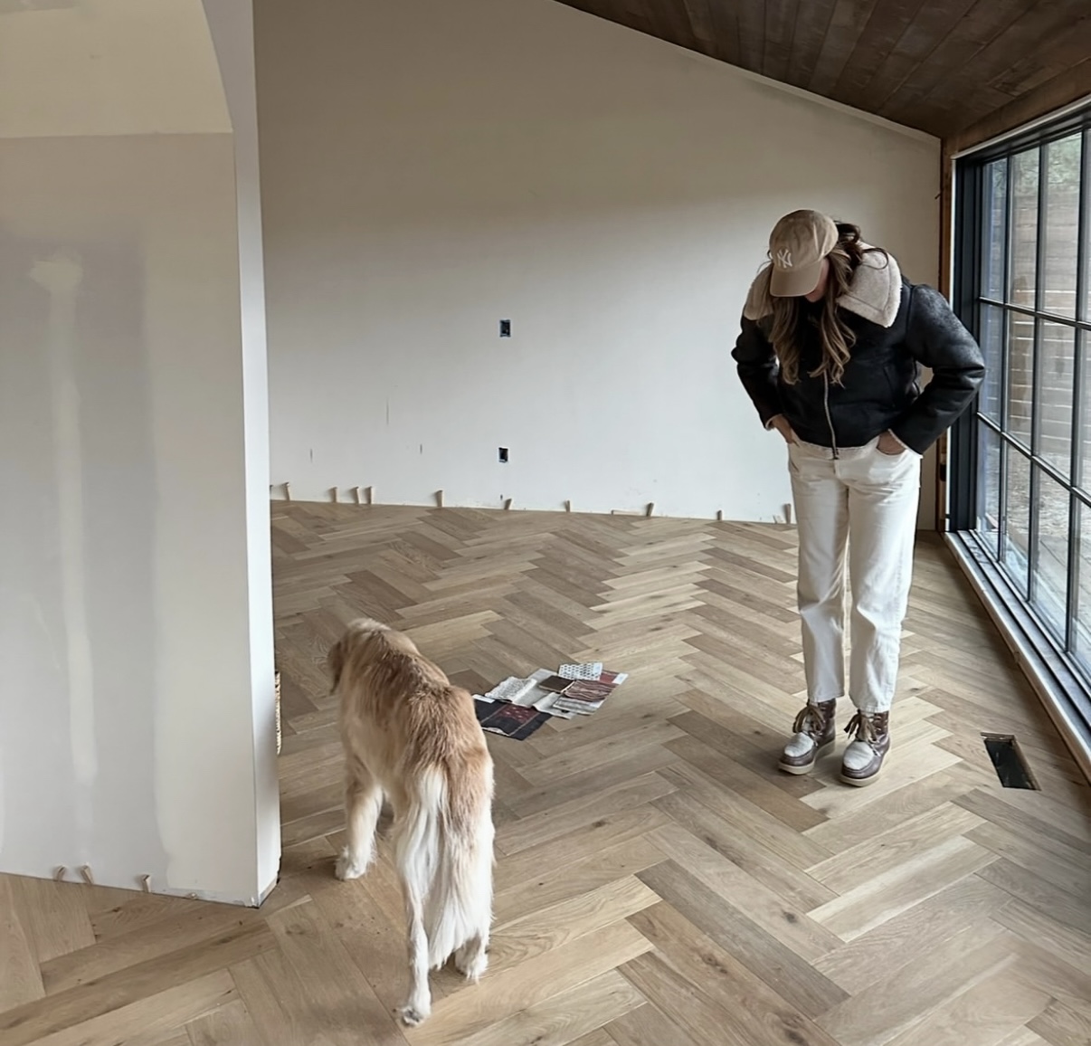 An in-progress design moment with herringbone oak flooring, swatches laid out for final selections, Lucy the golden retriever exploring, and Allison looking on thoughtfully.