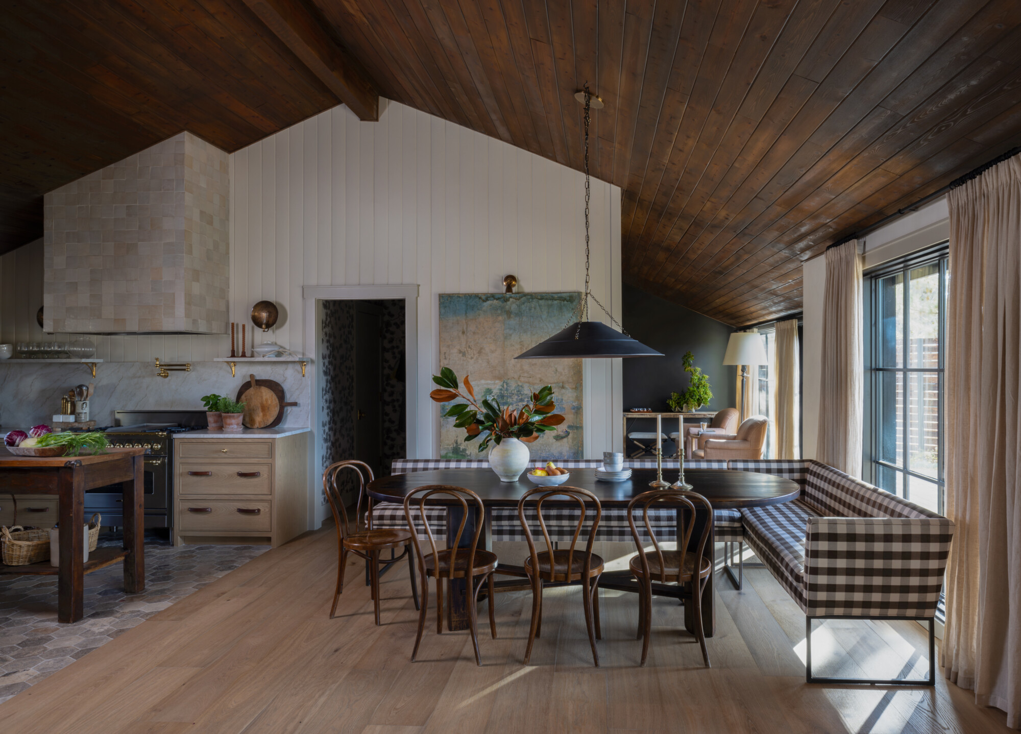 Tongue and groove ceiling with rustic wood finish above a cozy living space featuring a plaid sectional banquette, dark wood table, and bentwood chairs in a sun-filled dining nook.