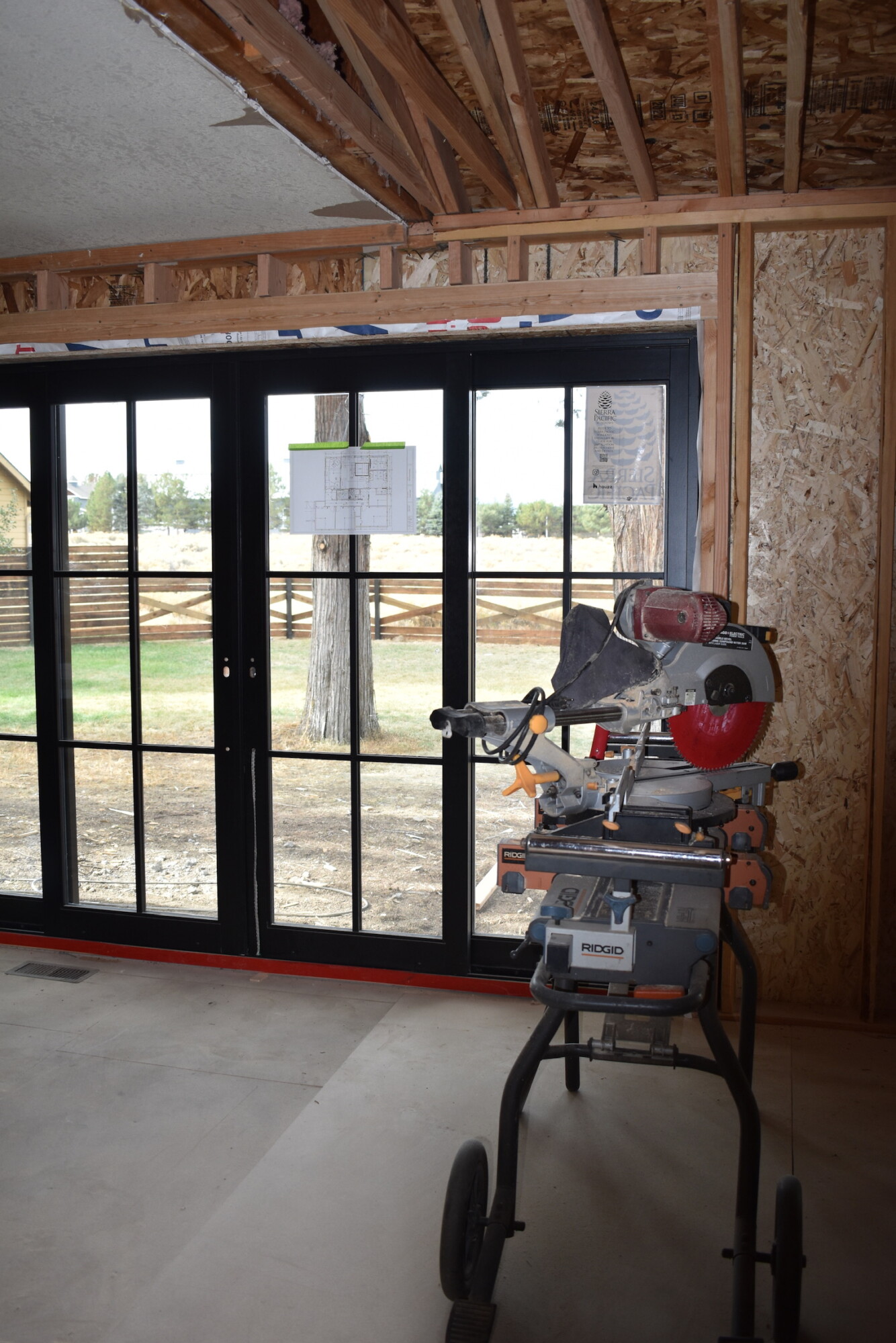 Framed black steel patio doors in construction, miter saw staged on site.