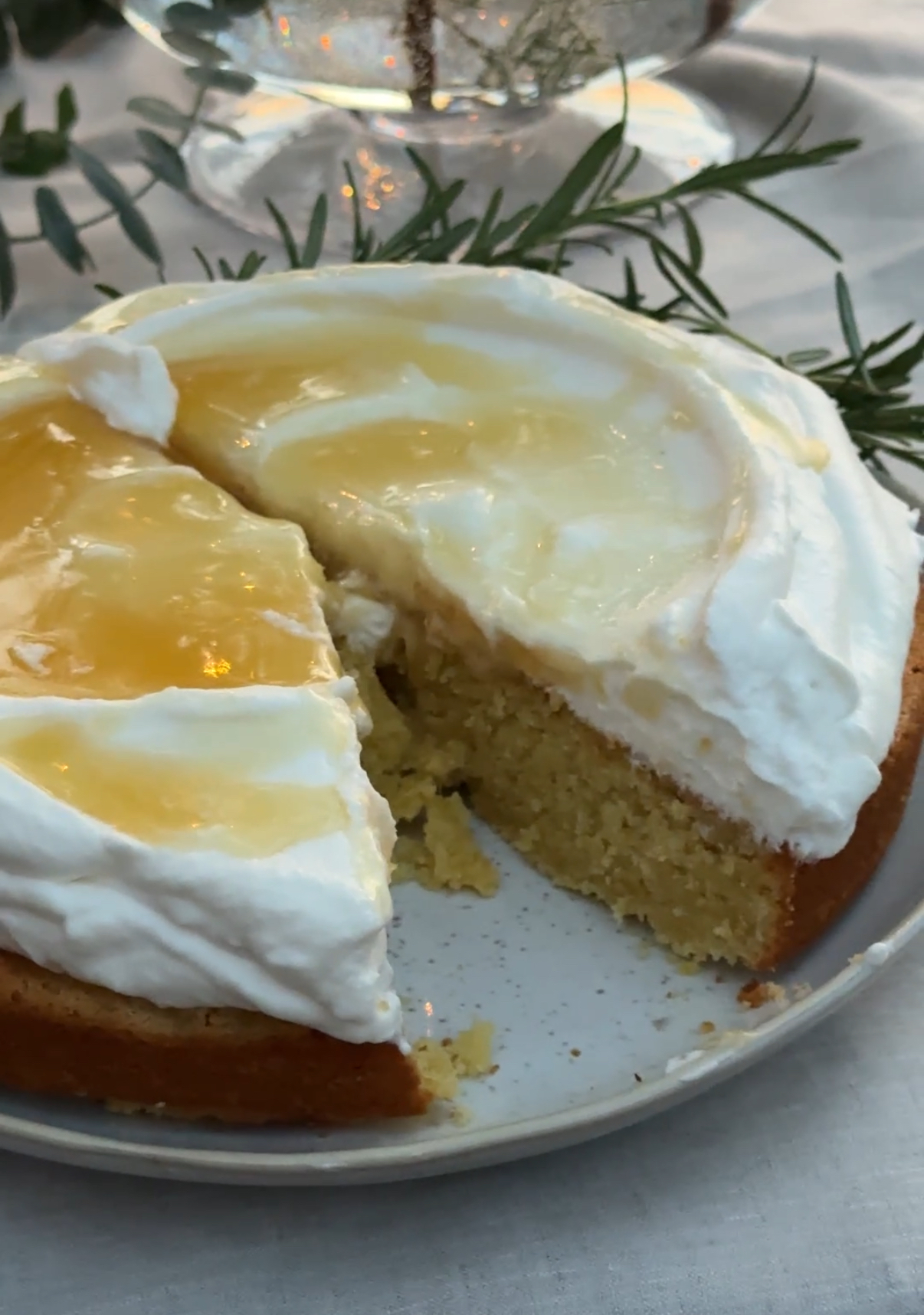A close-up of a lemon Amalfi cake topped with whipped cream and lemon glaze, with one slice cut out to reveal the moist golden interior.