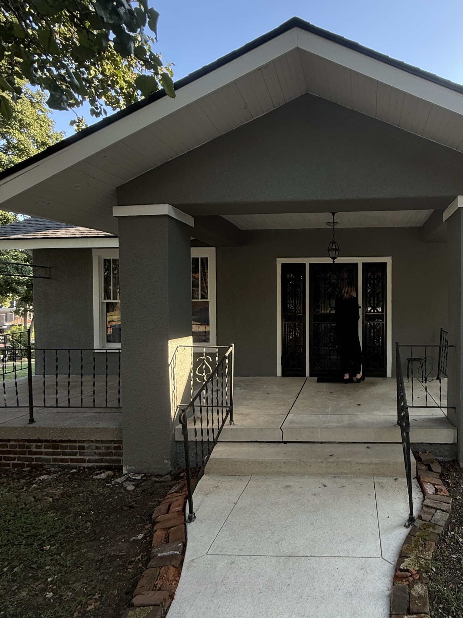 Historic Craftsman-style bungalow in downtown Columbia, TN with a deep gabled porch, charcoal stucco, white trim, original iron railings, and decorative double doors—captured in evening light during our “before” walkthrough.