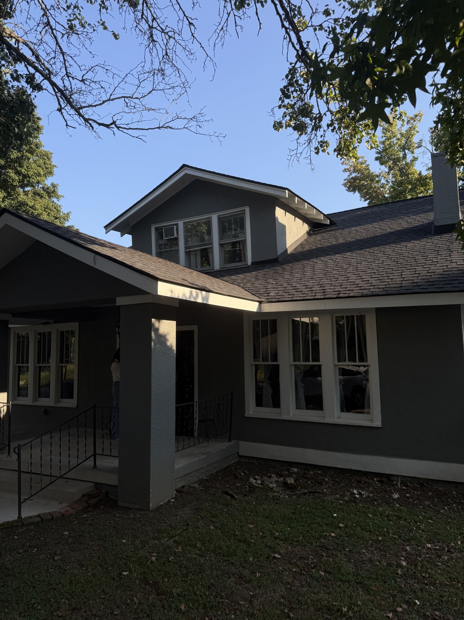 Pre-renovation Columbia, TN bungalow showing low-pitched roof with dormer, wraparound porch, original multi-pane windows, and mature trees framing the façade.