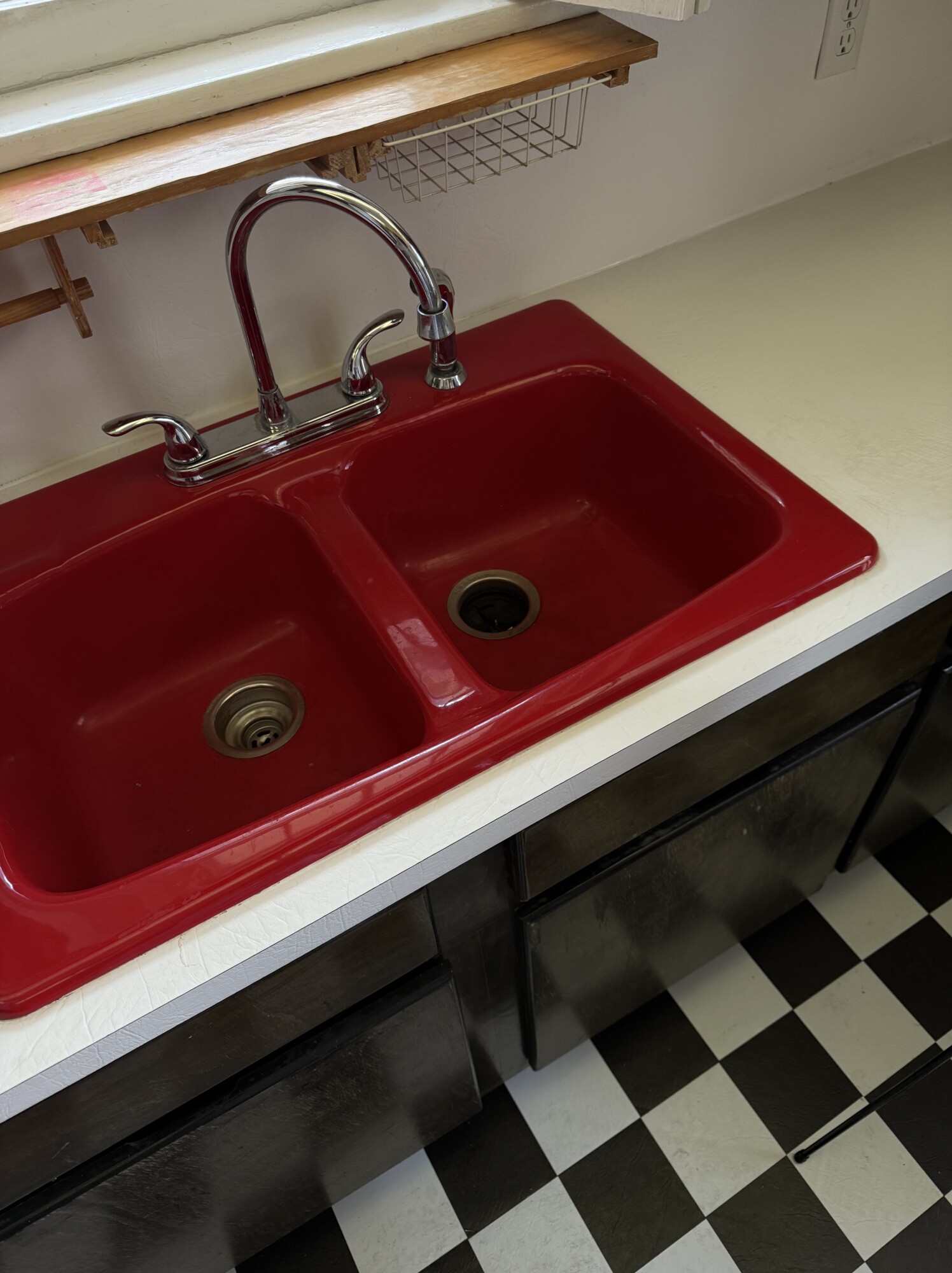 Vintage red double-basin kitchen sink with chrome faucet on white laminate counters and checkerboard floor — before renovation.