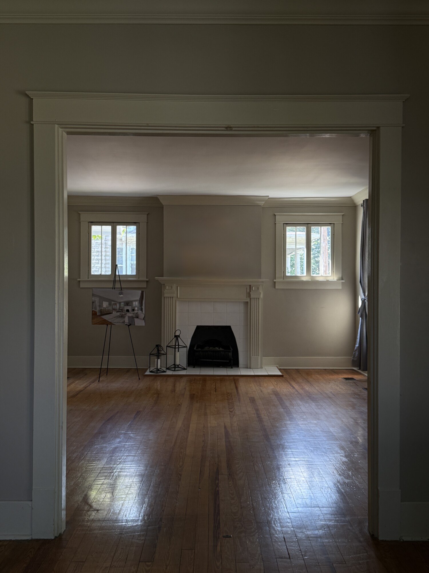 View through wide cased opening to living room with tiled fireplace, hardwood floors, and twin high windows — before.