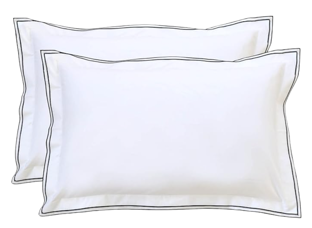 Pair of white pillow shams with thin black piping and flange—classic hotel bedding.