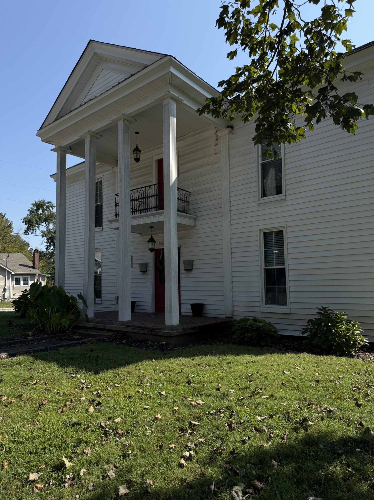 White two-story farmhouse with tall Greek-revival columns and a red front door, viewed from the lawn on a sunny day.