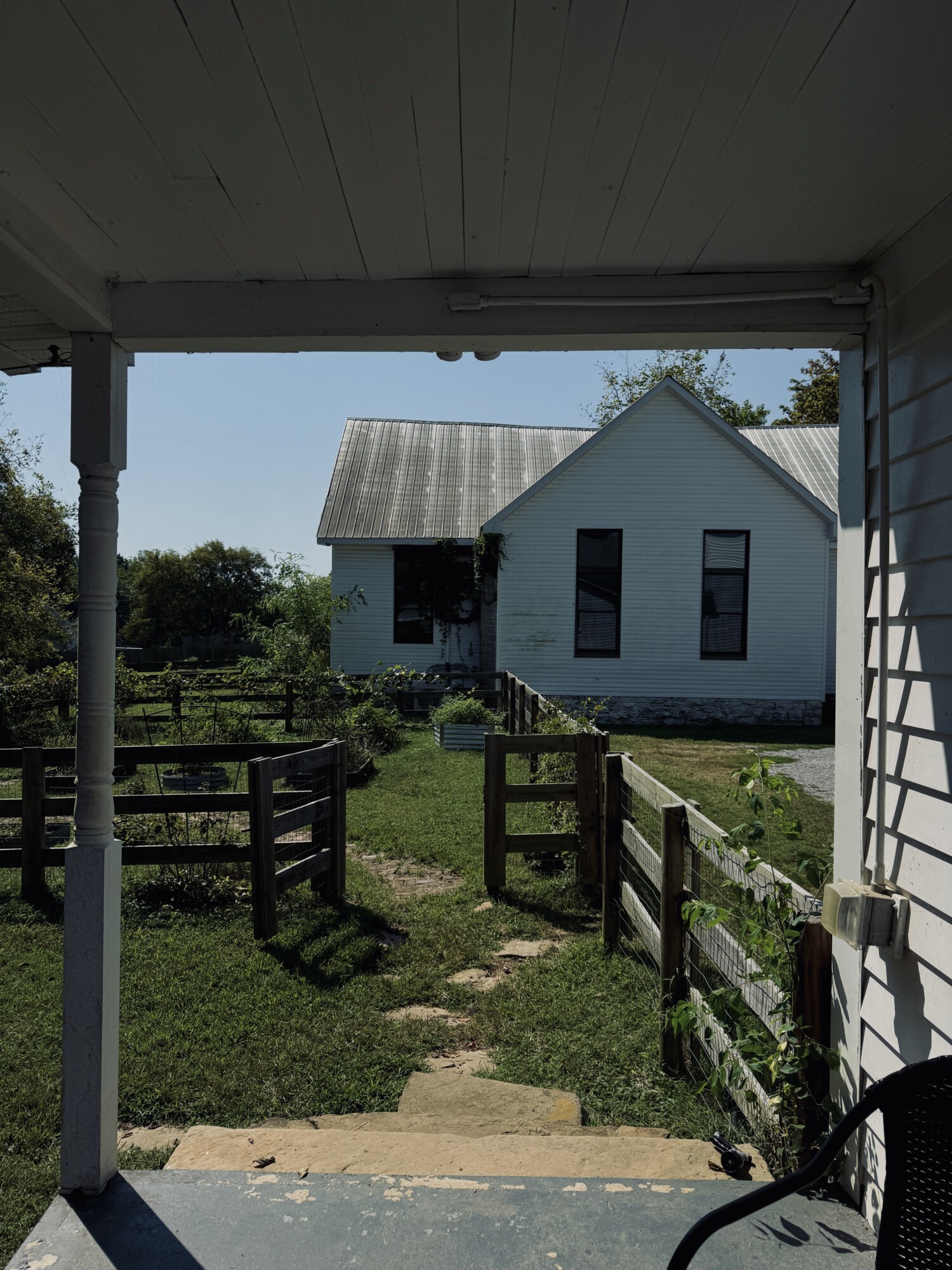 View from back porch toward a fenced vegetable garden and a separate white church-style outbuilding.