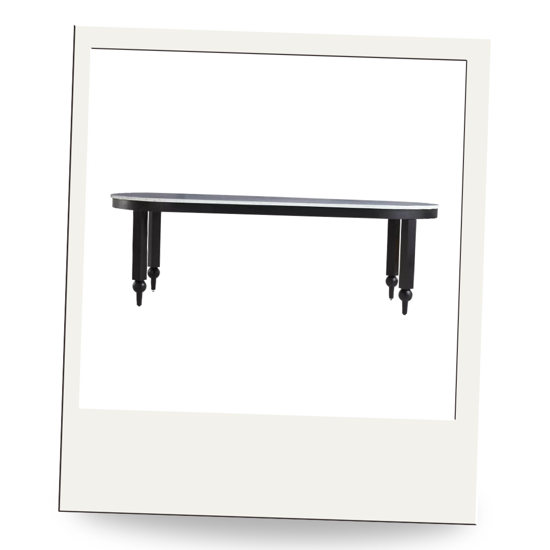 Black oval dining table with sculptural turned legs on a clean white background, framed in a vintage-style Polaroid border.