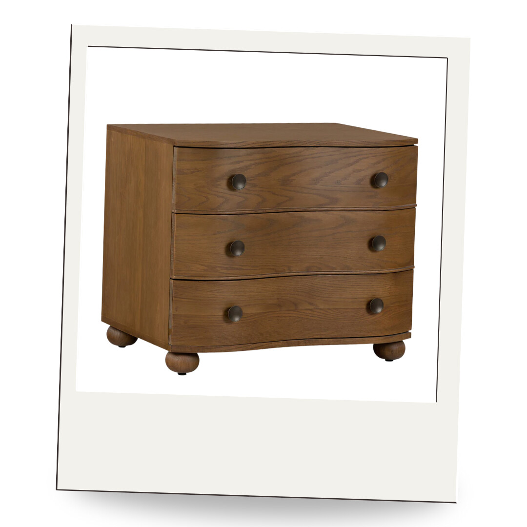 A three-drawer wooden dresser with soft curves, bun feet, and dark knobs, blending traditional craftsmanship with a timeless silhouette.