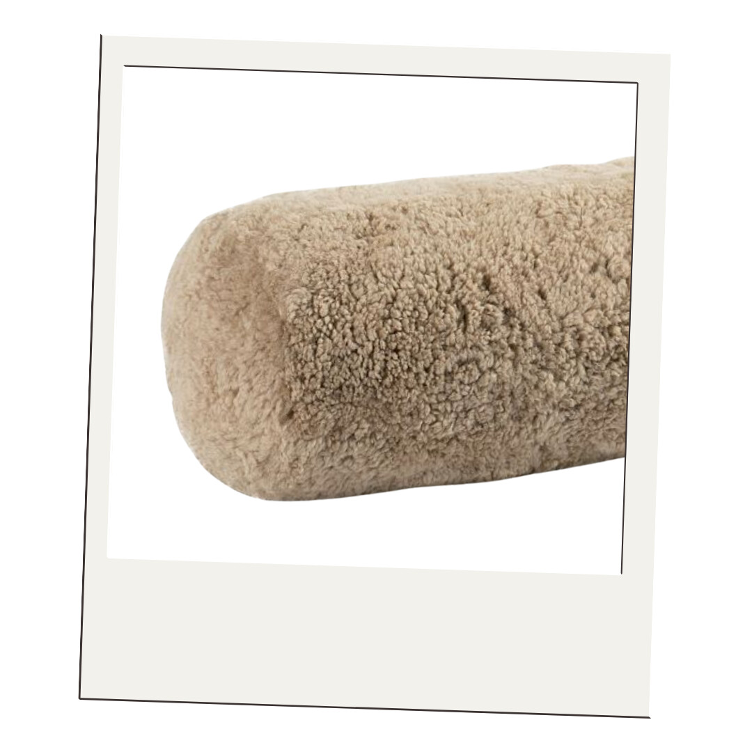 A cozy, taupe shearling bolster pillow adding texture and warmth to any bed or reading nook.
