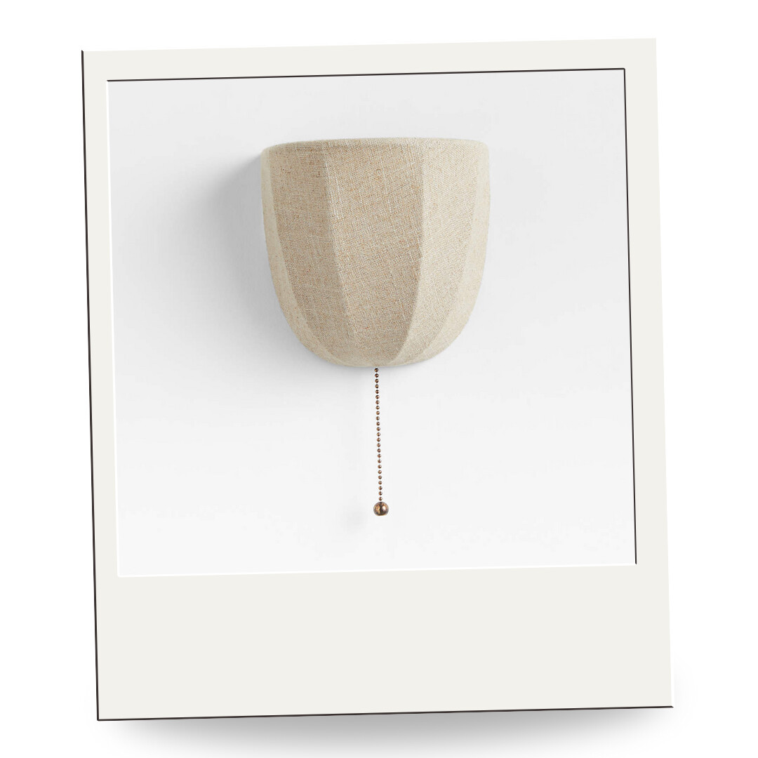 Sculptural linen wall sconce with pleated shade and brass pull chain, offering soft ambient light with a handcrafted feel.