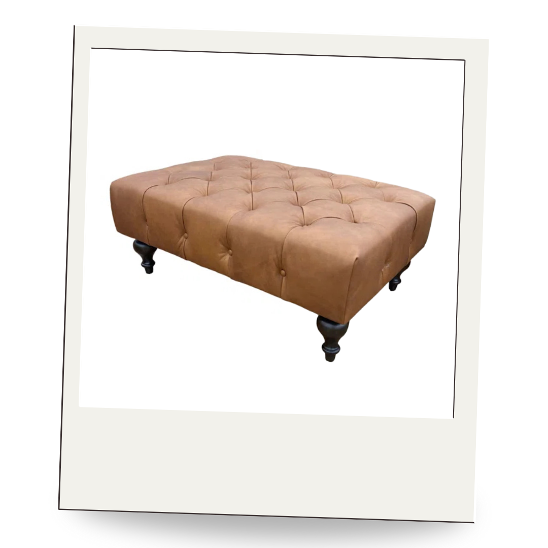 Rectangular tufted leather ottoman with dark turned legs, perfect for layering trays, books, or cozy throws in a living room.