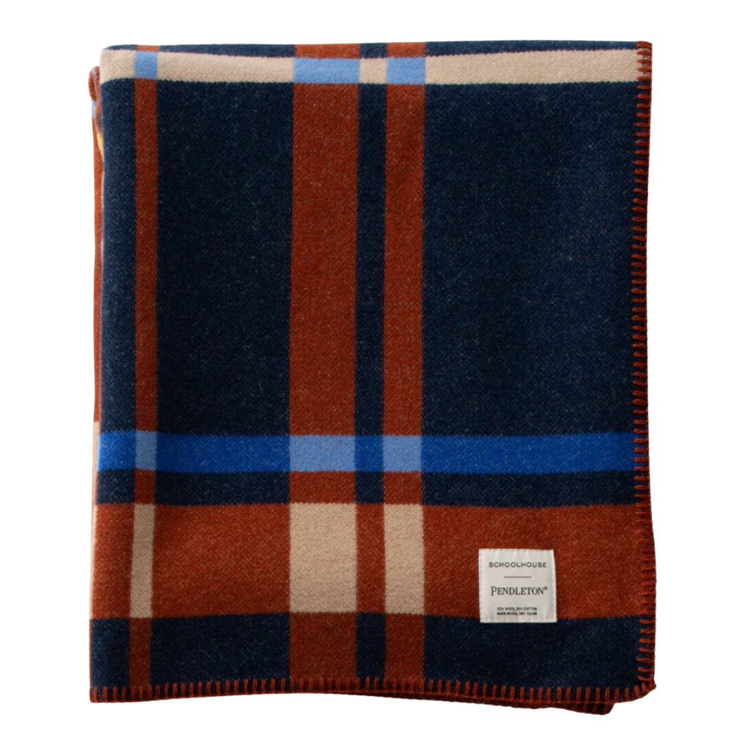 Plaid Pendleton wool blanket in rust, navy, and blue tones with a stitched edge—perfect for cozy winter nights.