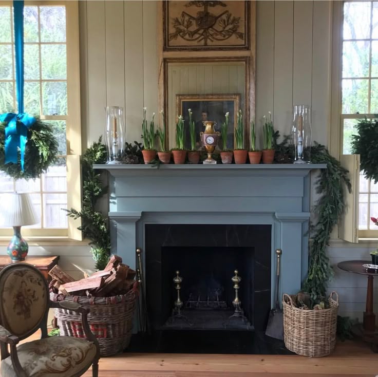 Classic living room fireplace decorated with potted paperwhites, evergreen garlands, and wreaths, surrounded by woven baskets filled with firewood.