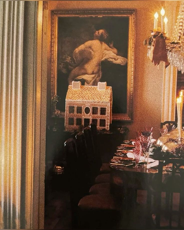 Moody, candlelit dining room featuring a gingerbread house centerpiece, ornate artwork, and a holiday tablescape with gold accents.
