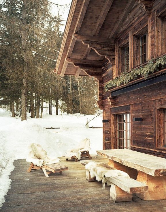 Cozy mountain cabin porch in Aspen with snow-covered ground, wood exterior, and sheepskin throws laid out in the winter sun.