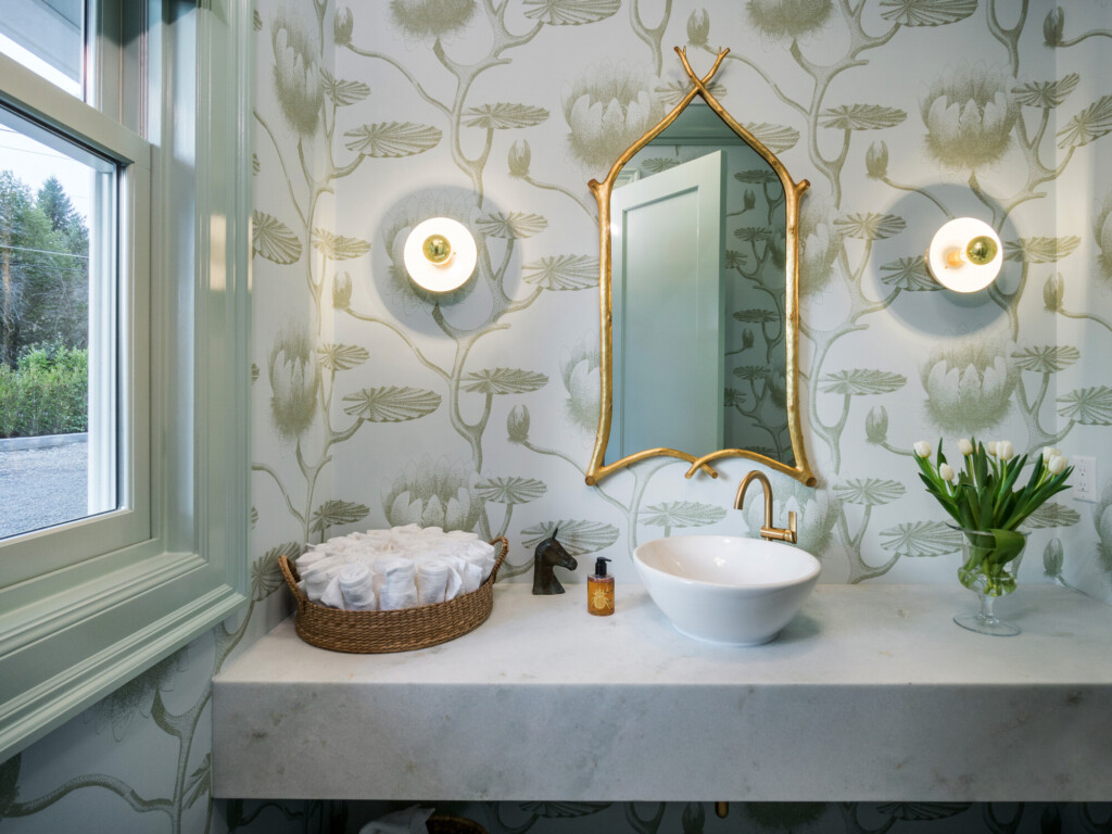 Powder bathroom with botanical wallpaper, gold arched mirror, marble vanity, vessel sink, and brass faucet.