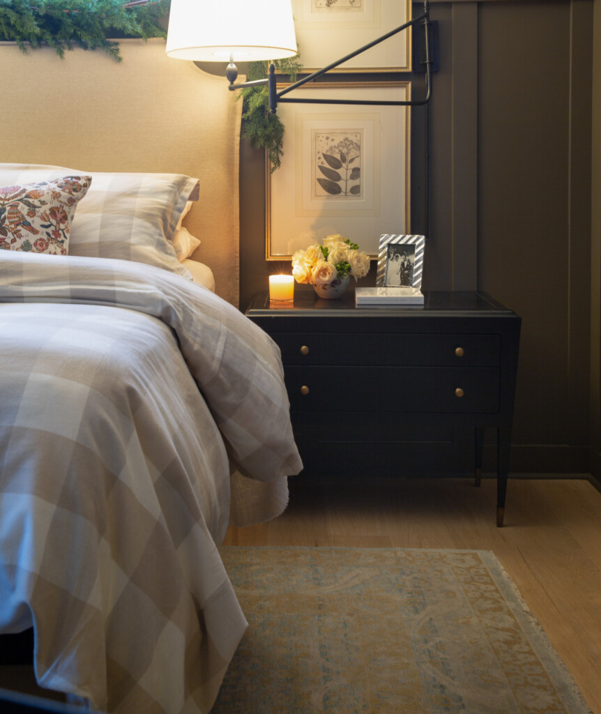 Cozy bedroom with upholstered headboard, plaid bedding, black nightstand, and holiday greenery decor.