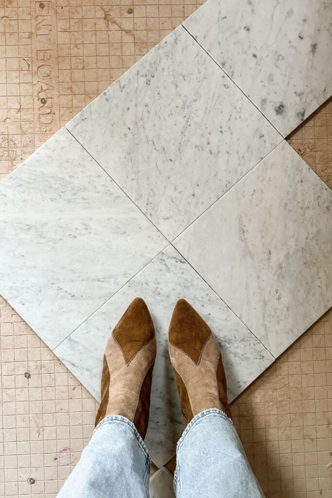 Carrara marble floor tiles in a diamond pattern during installation with boots visible for scale.