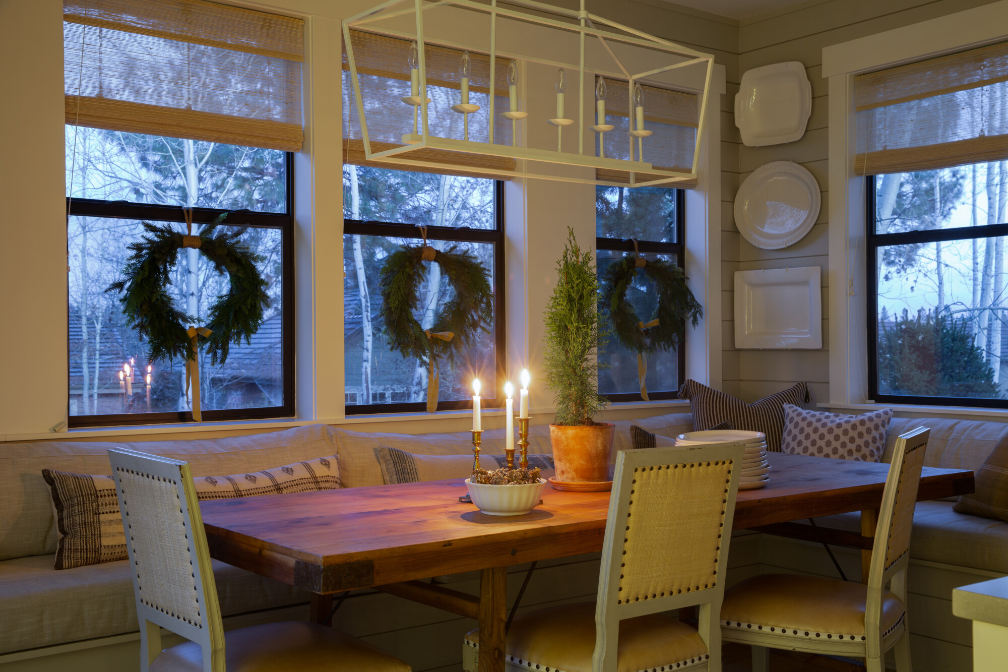 Breakfast nook with built-in bench seating, holiday wreaths on the windows, candlelit centerpiece, and ceramic plate wall decor.
