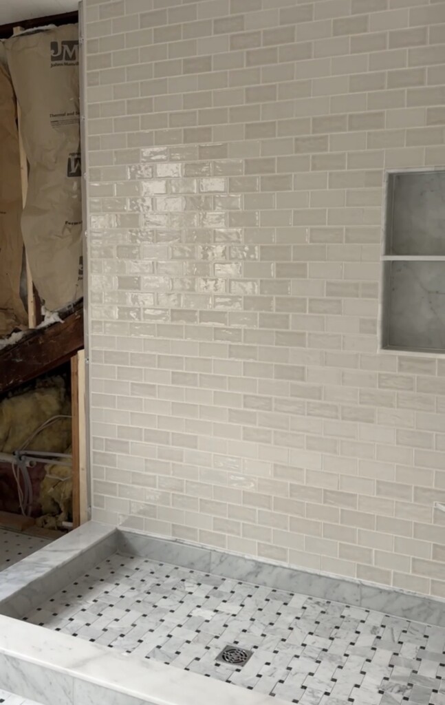 Upstairs bathroom shower with classic marble basketweave tile floor, Carrara marble curb, and soft neutral ceramic subway tile walls at the Sixth Street Bungalow in Columbia, Tennessee.