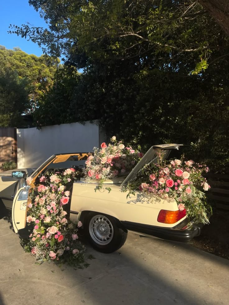 Vintage convertible car decorated with cascading pink and blush floral arrangements, parked outdoors in soft afternoon light, creating a romantic Galentine’s Day party aesthetic.