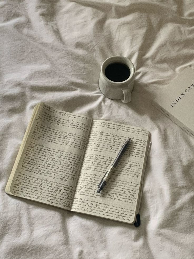 Open journal filled with handwritten notes resting on rumpled white bedding, with a pen laid across the pages, a ceramic mug of coffee nearby, and a soft, quiet morning atmosphere.