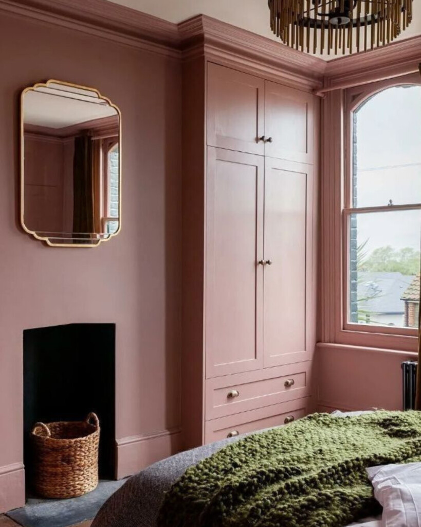 Dusty rose bedroom with built-in cabinetry and crown molding, featuring a soft pink wall color, green textured bedding, and warm wood accents.