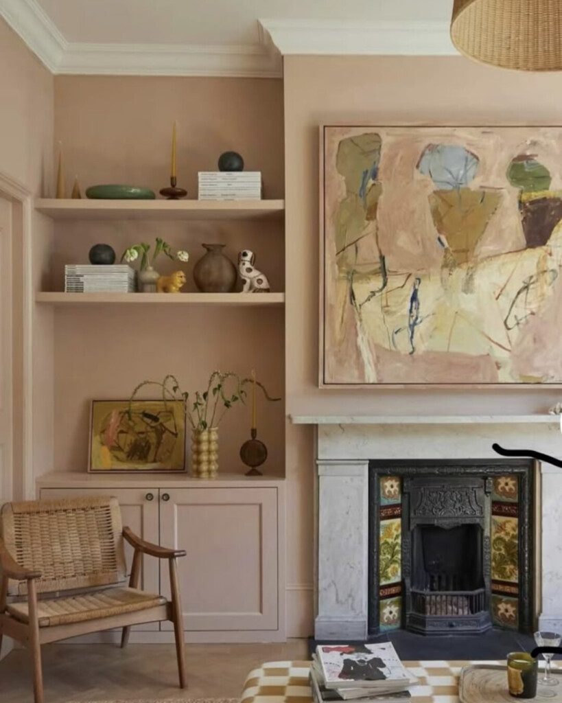 Muted pink living room with built-in shelving and fireplace, featuring collected ceramics, artwork, and a soft neutral blush paint color as the backdrop.