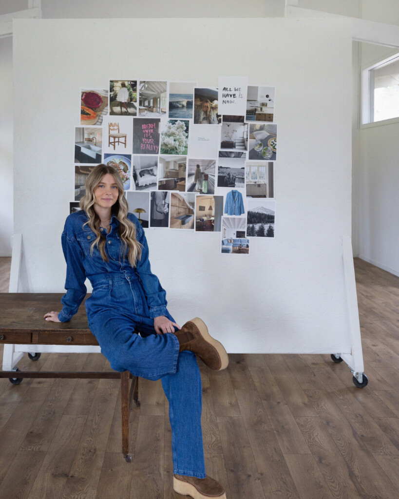 Kaylei: Woman in a denim jumpsuit sitting on a wooden bench in front of a large rolling inspiration board covered in design, fashion, and lifestyle imagery.