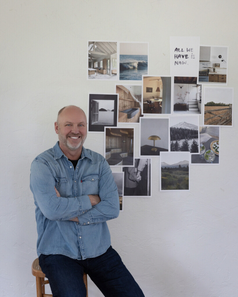 Derrick: Man in a light denim button-down shirt and dark jeans sitting on a wooden stool with arms crossed, smiling in front of a wall collage of interior and landscape inspiration images.