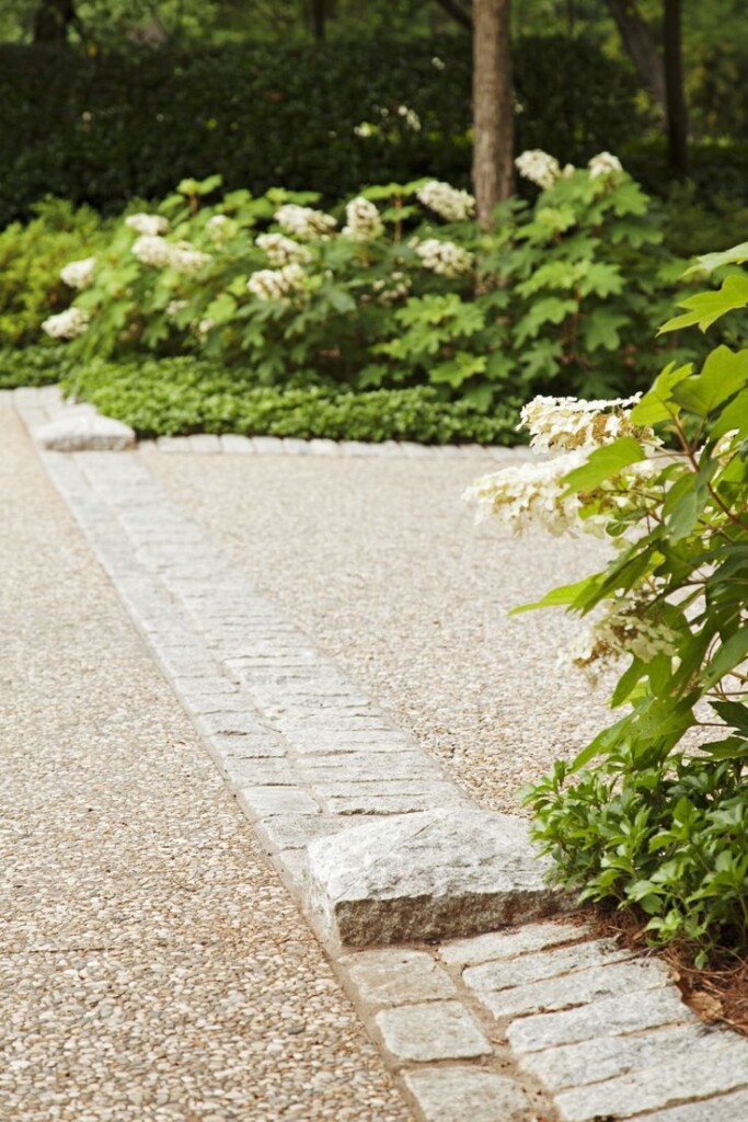 Pea gravel garden patio with stone curbstone edging, cobblestone detail, and layered hydrangea and hedge landscaping in a lush backyard setting