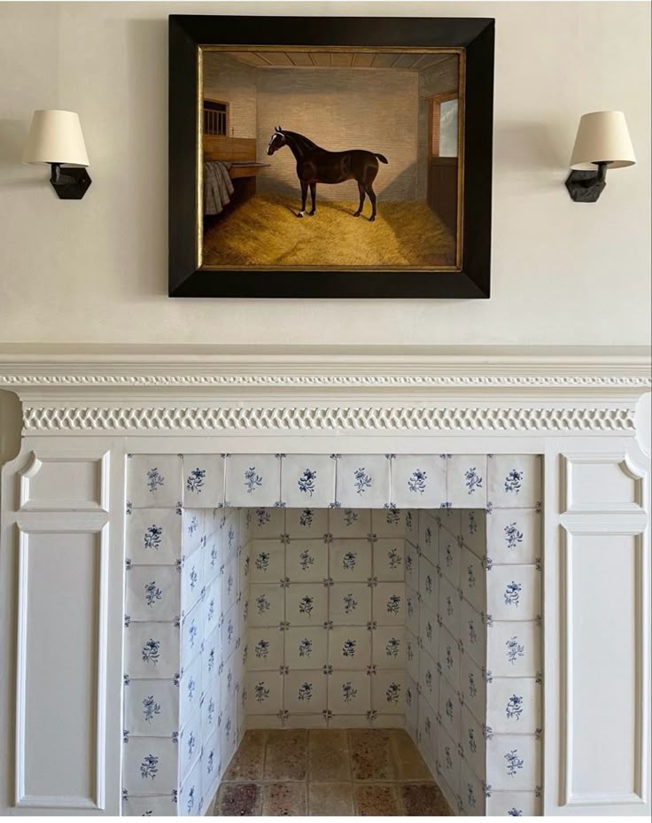 Traditional white fireplace surround with blue and white Delft tile interior, decorative wall sconces, and framed horse artwork above mantel.