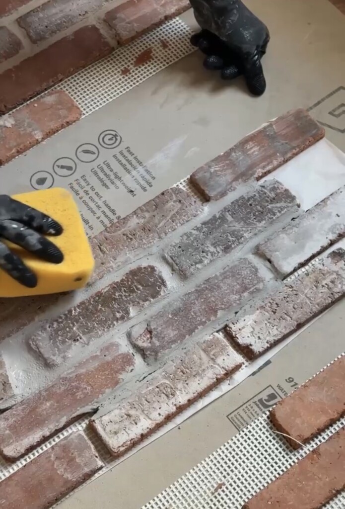 Hands applying and smoothing grout over brick veneer tiles during installation, creating a softened, aged look for a kitchen floor.