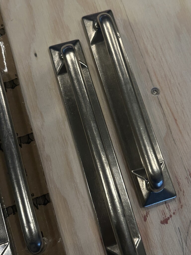 Close-up of Rocky Mountain Hardware cabinet pulls in a brushed metal finish displayed on a wood surface before installation.