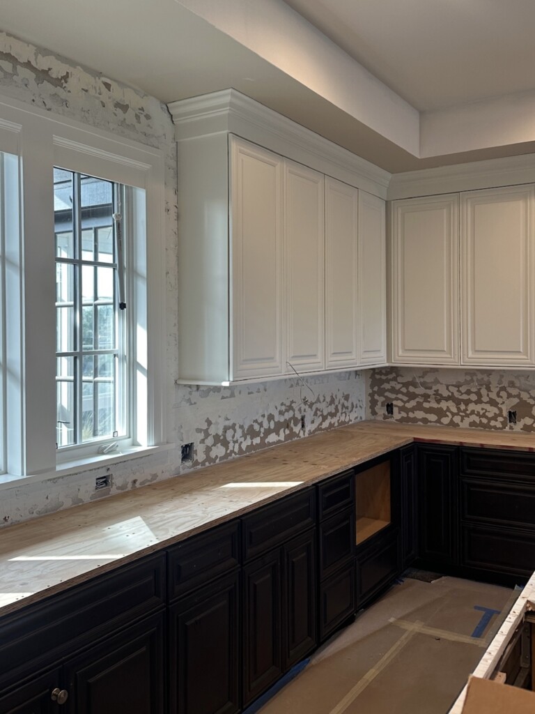 Kitchen renovation in progress with freshly painted white upper cabinets, original dark mahogany lower cabinets, and countertops removed for upgrade.